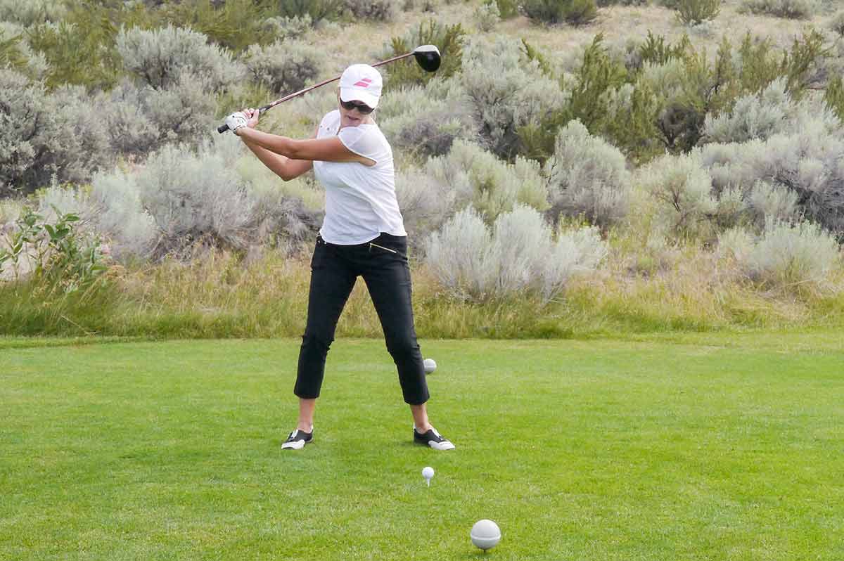 A woman over 50 confidently striking a golf ball with a driver, mid-swing on a sunny course—her form strong and focused, capturing the energy and precision of the moment.