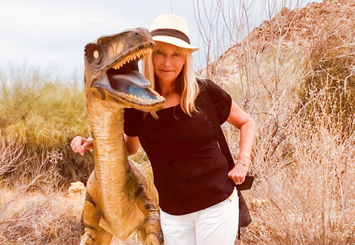 confident mature woman standing next to a dinosaur statue