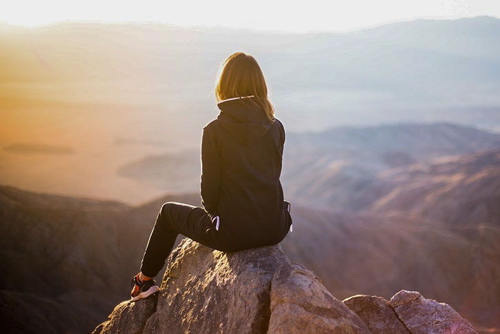 mature woman sitting on a rock on top of a mountain thinking